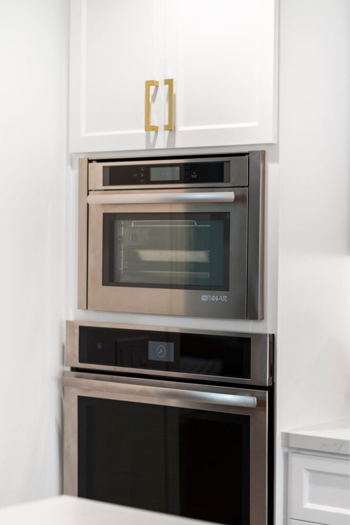 Stacked stainless wall ovens built into white cabinetry with brass rectangular pulls.