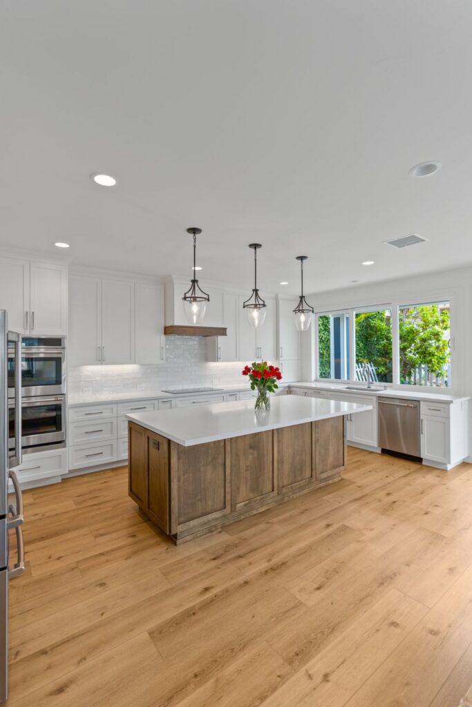 White kitchen with wood island, quartz counters, pendant lights, stainless appliances and wide window over the sink.