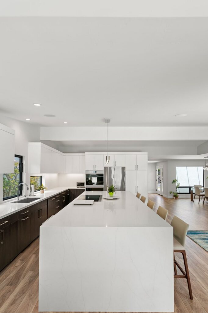 Open kitchen with white waterfall island, two-tone cabinetry, stainless appliances and wood-look flooring.