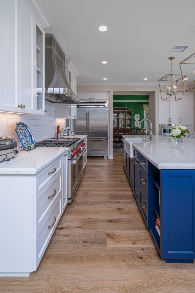 Two-cook kitchen with blue island, white cabinetry, stainless range and refrigerator, and wide-plank wood flooring.
