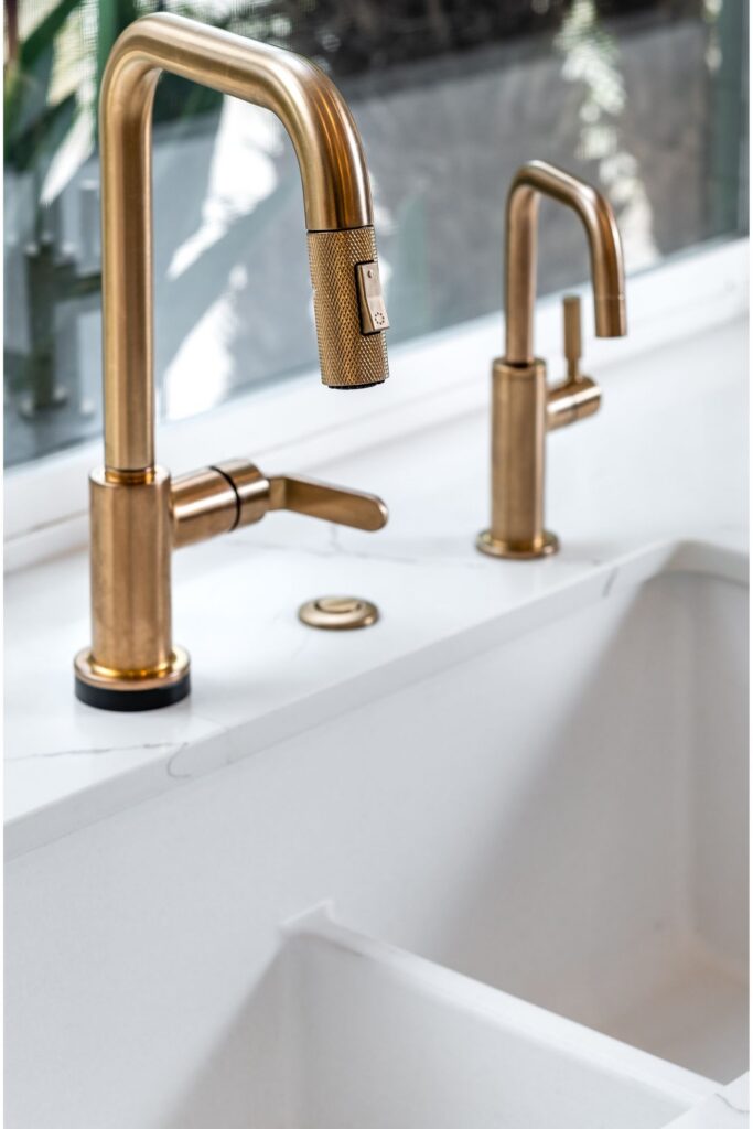 Brushed brass kitchen faucet and secondary faucet mounted beside a white apron-front sink.