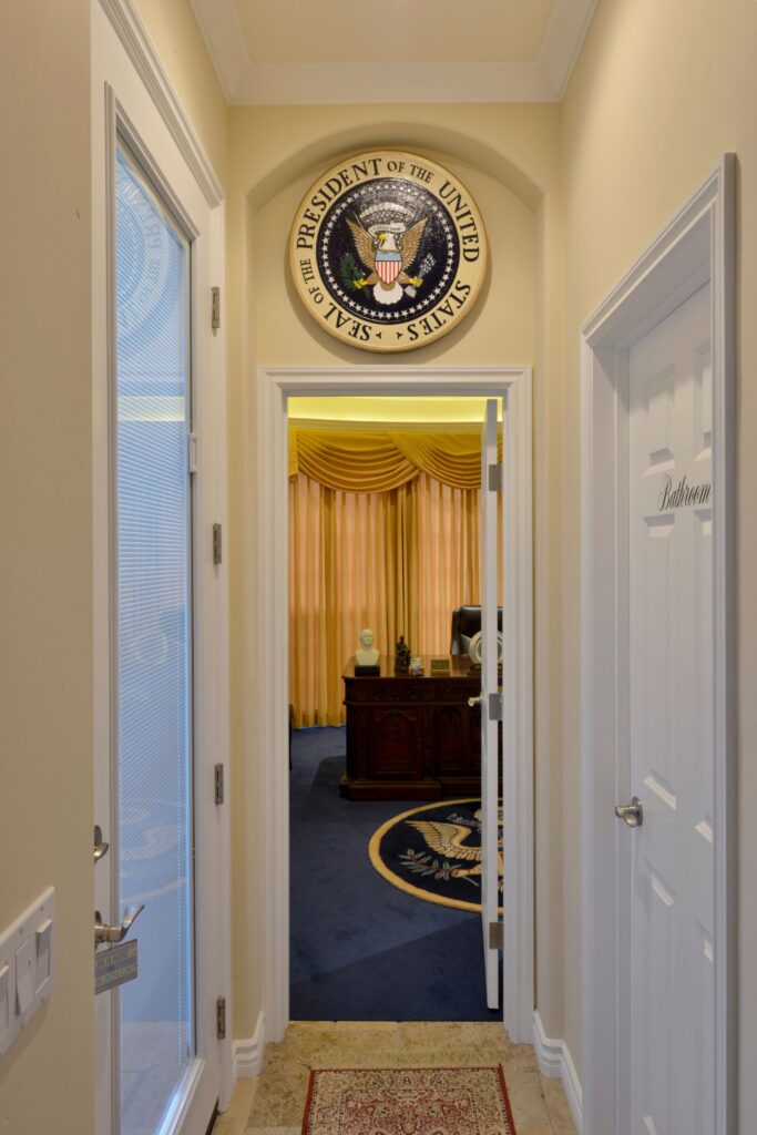 Hallway with presidential seal above an office doorway, white trim, tiled floor and adjacent bathroom door.