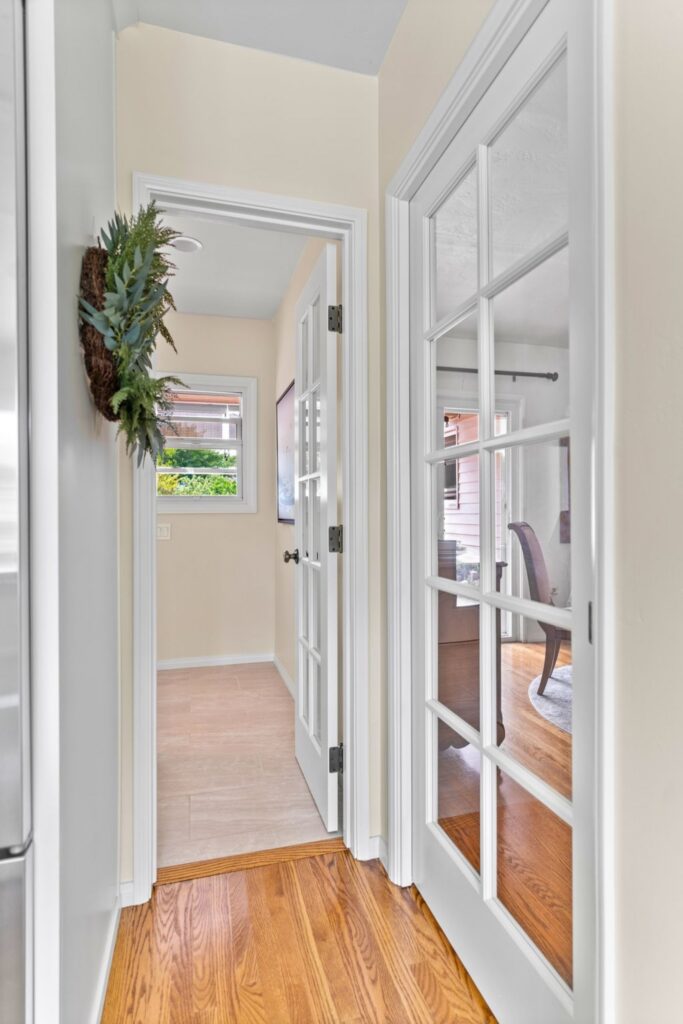 Remodeled hallway with wood flooring, glass-paneled interior doors, white trim and adjoining tiled utility area.