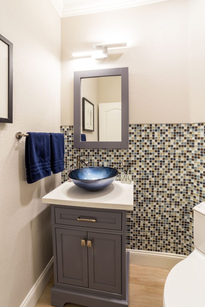 Powder room with gray vanity, blue vessel sink, mosaic tile wainscoting and rectangular framed mirror.