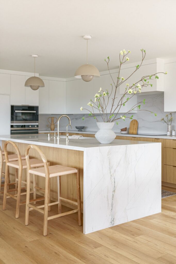 Kitchen with waterfall-edge island, light wood cabinetry, white upper cabinets and dome pendant lighting