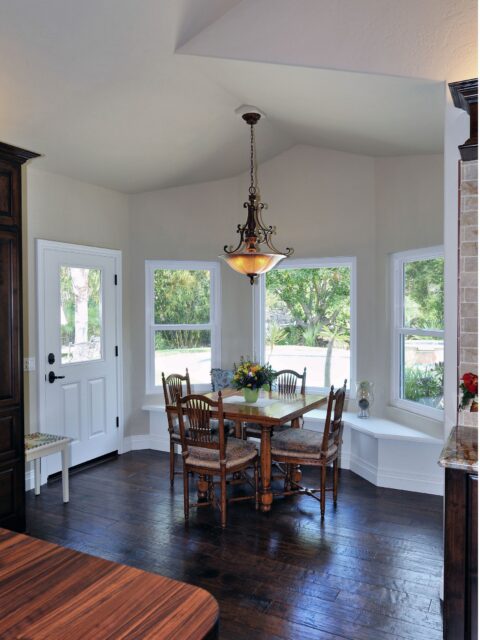 Breakfast nook with wraparound windows, built-in bench seating, dark wood floor and decorative chandelier