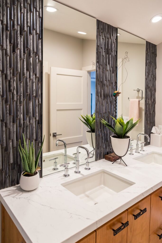 Double bathroom vanity with wood cabinetry, veined white countertop, chrome faucets and dark textured tile accents