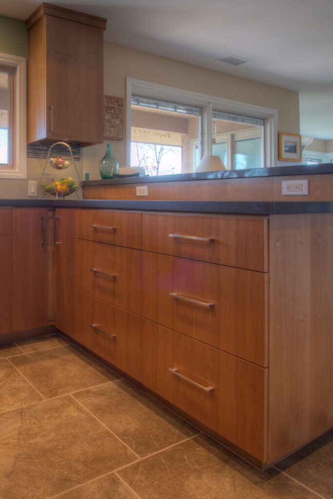 Wood kitchen cabinetry with deep drawers, gray counters, built-in outlets and large-format tile flooring
