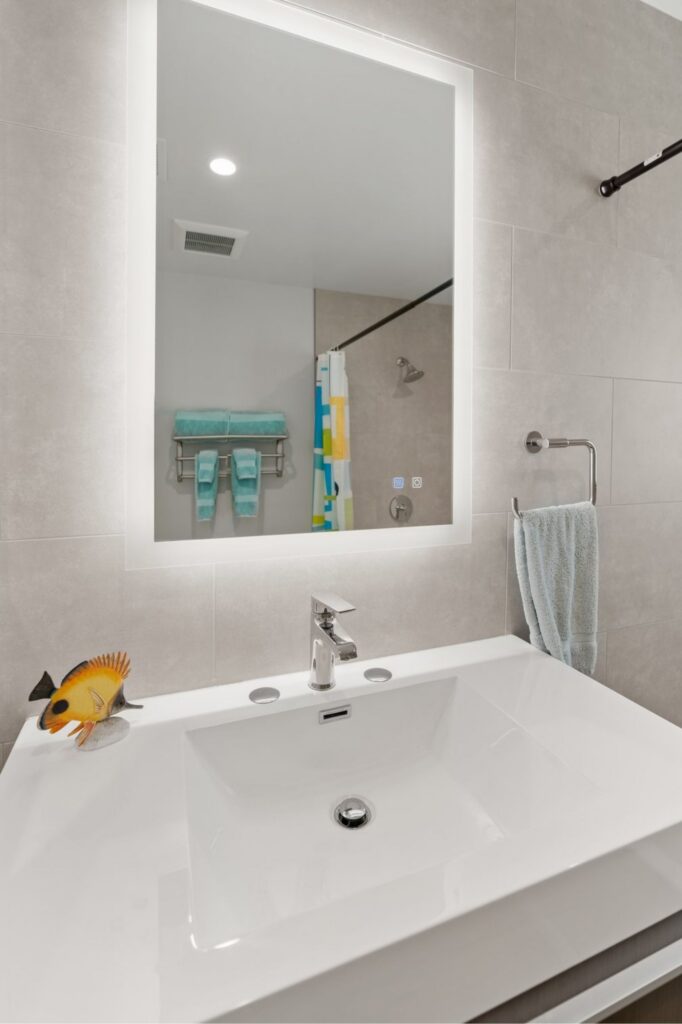 Bathroom vanity with integrated white sink, illuminated mirror, gray wall tile and chrome fixtures.