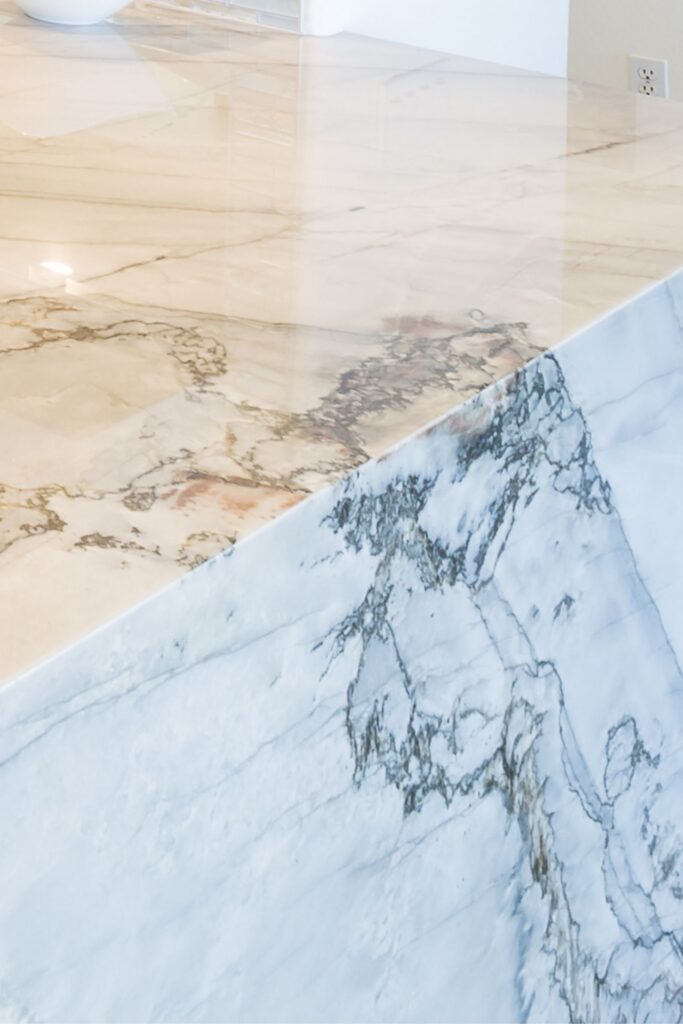 Close-up of light veined stone countertop with waterfall edge and prominent gray and taupe veining.