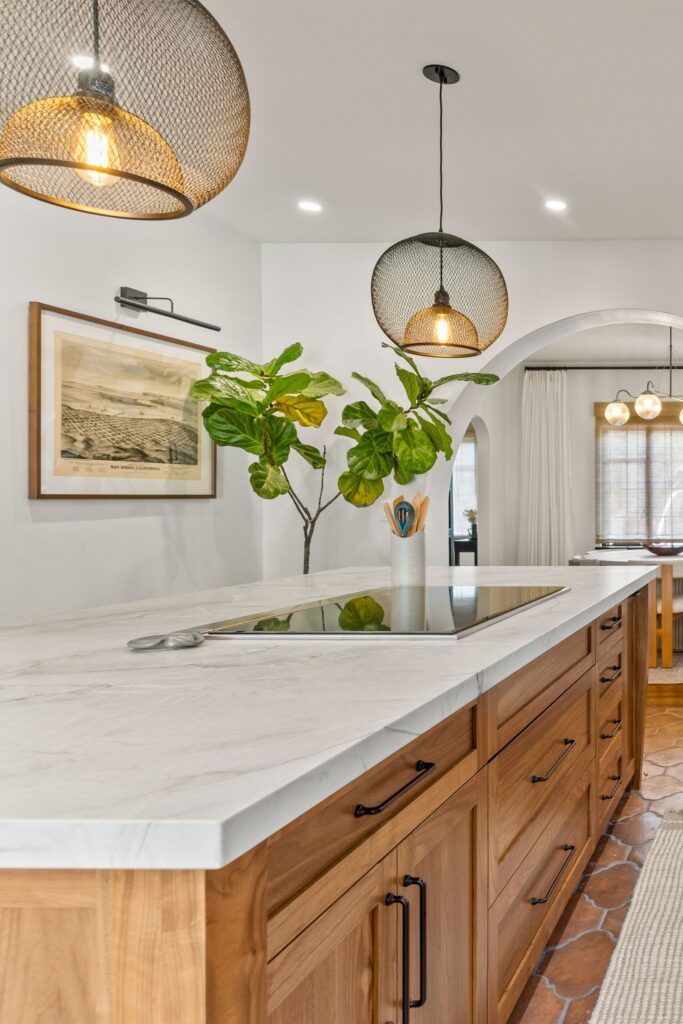 Wood kitchen island with white veined countertop, integrated cooktop, black mesh pendants and terracotta tile flooring