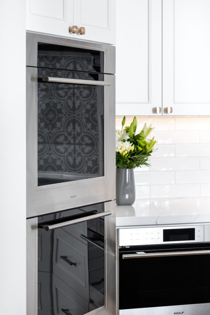 Stainless steel wall ovens built into white cabinetry beside a white subway tile backsplash.