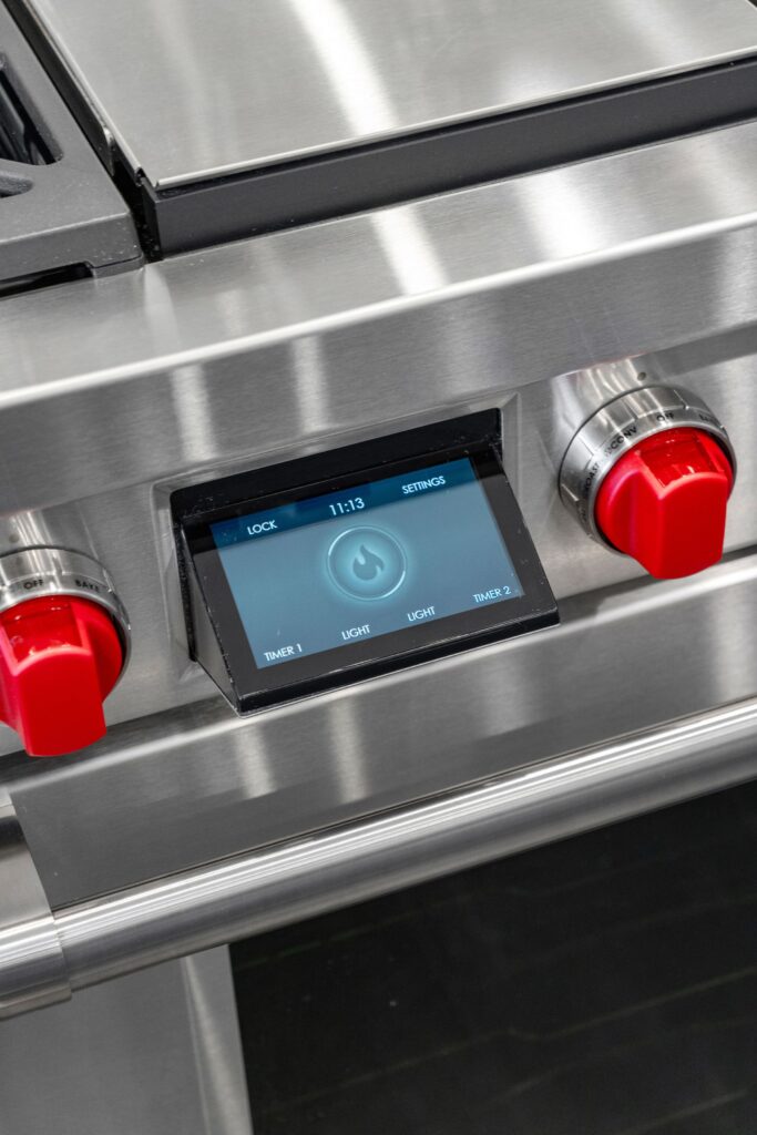 Stainless steel range control panel with touchscreen display and signature red knobs.