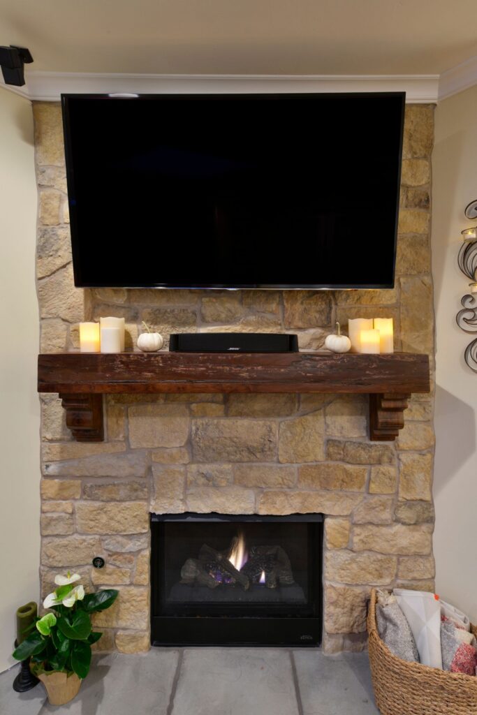 Stone fireplace with dark wood mantel, mounted television, soundbar and gas firebox.