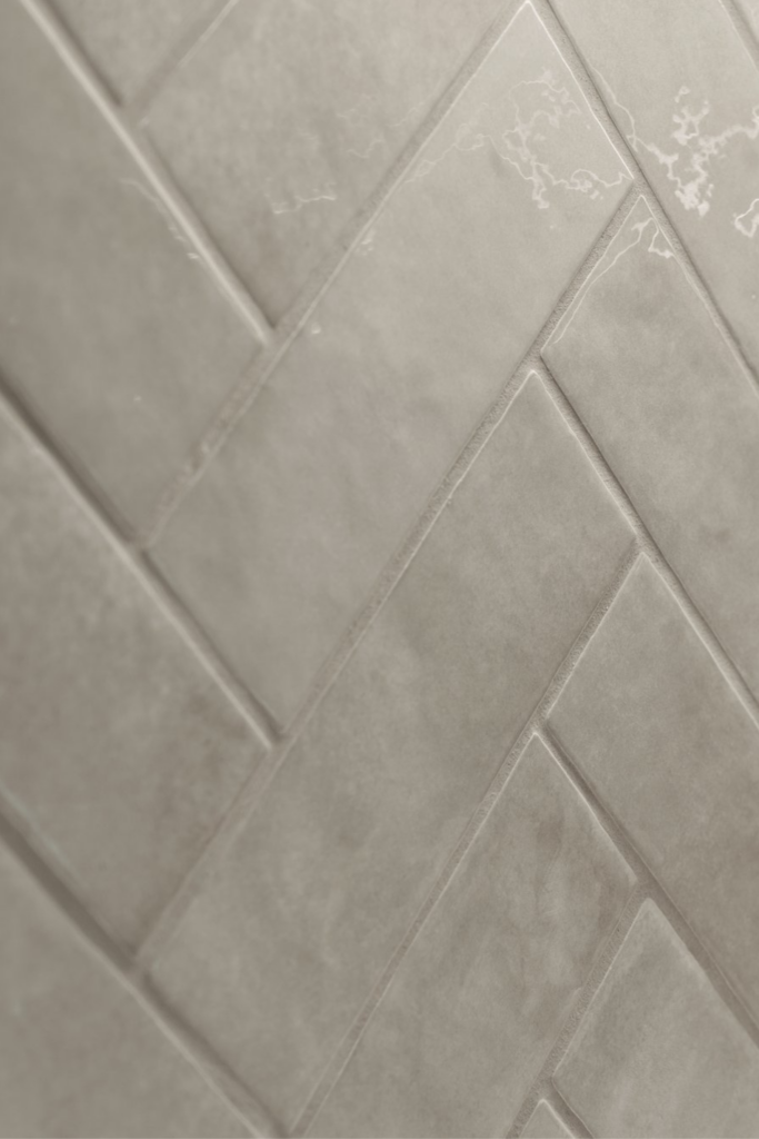 Close-up of light gray herringbone tile backsplash with subtle tonal variation.
