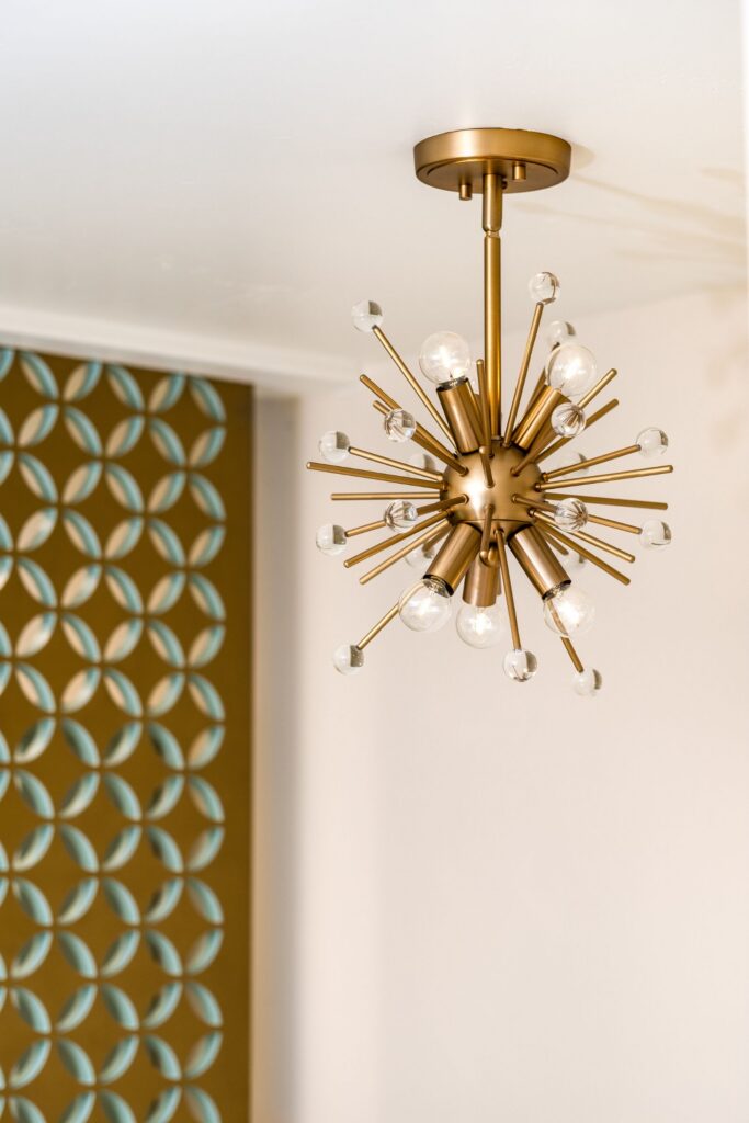 Brass starburst ceiling light with exposed bulbs beside decorative patterned wall panel