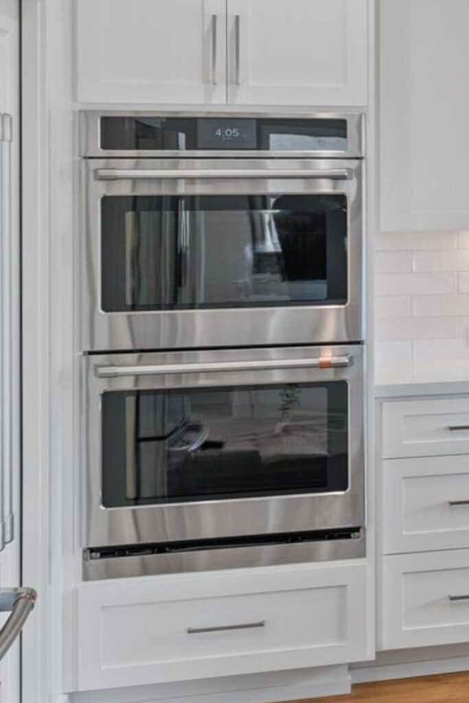 Stacked stainless wall ovens integrated into white shaker cabinetry with brushed metal pulls.