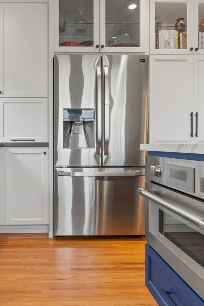 Stainless refrigerator surrounded by tall white pantry cabinets and glass-front display storage above.