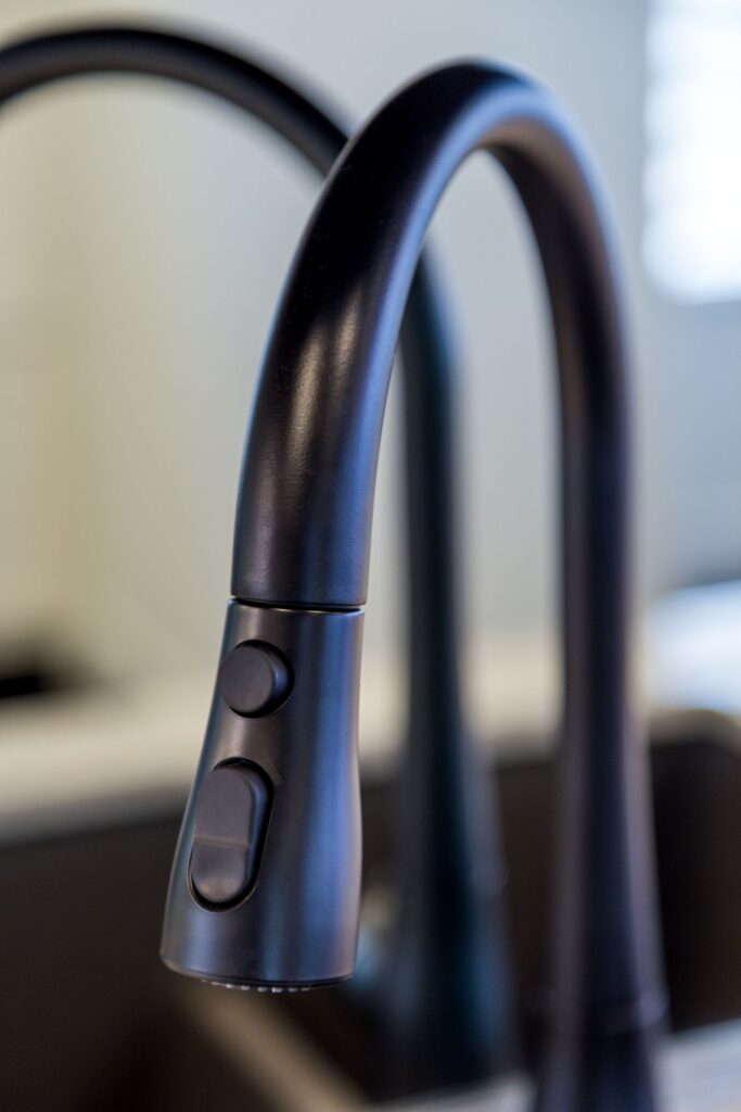 Matte black pull-down kitchen faucet with integrated controls above a dark sink.