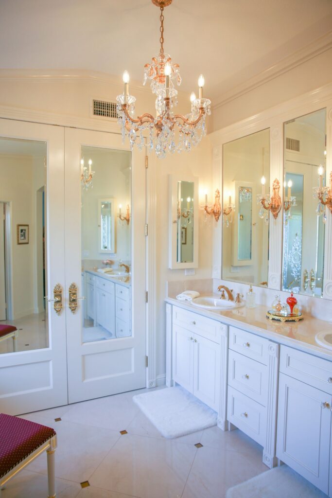 Carlsbad primary bathroom with white double vanity, mirrored doors, crystal chandelier and gold-accented lighting.