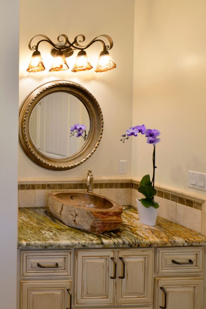 Powder room vanity with stone vessel sink, granite counter, round framed mirror and four-light wall fixture.