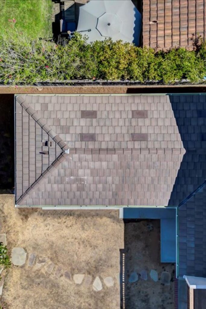 Aerial view of remodeled roof addition with shingle roofing, adjoining rooflines and rear yard below.