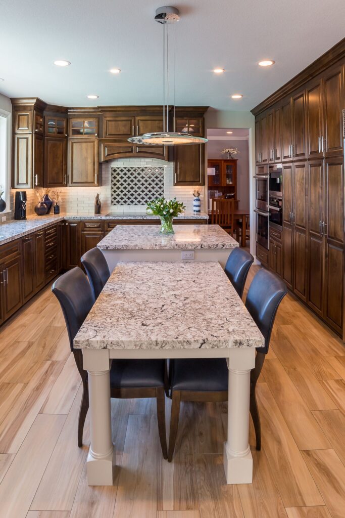 Kitchen remodel with dark wood cabinetry, granite counters, two-level island, pendant light and stainless appliances.