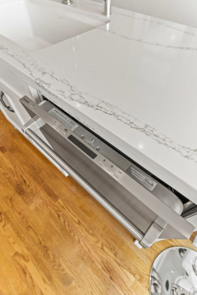 Stainless dishwasher installed beneath a veined white kitchen counter and integrated sink.