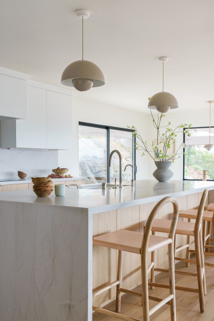 Kitchen island with integrated sink, light wood cabinetry, white counters and oversized dome pendant lights