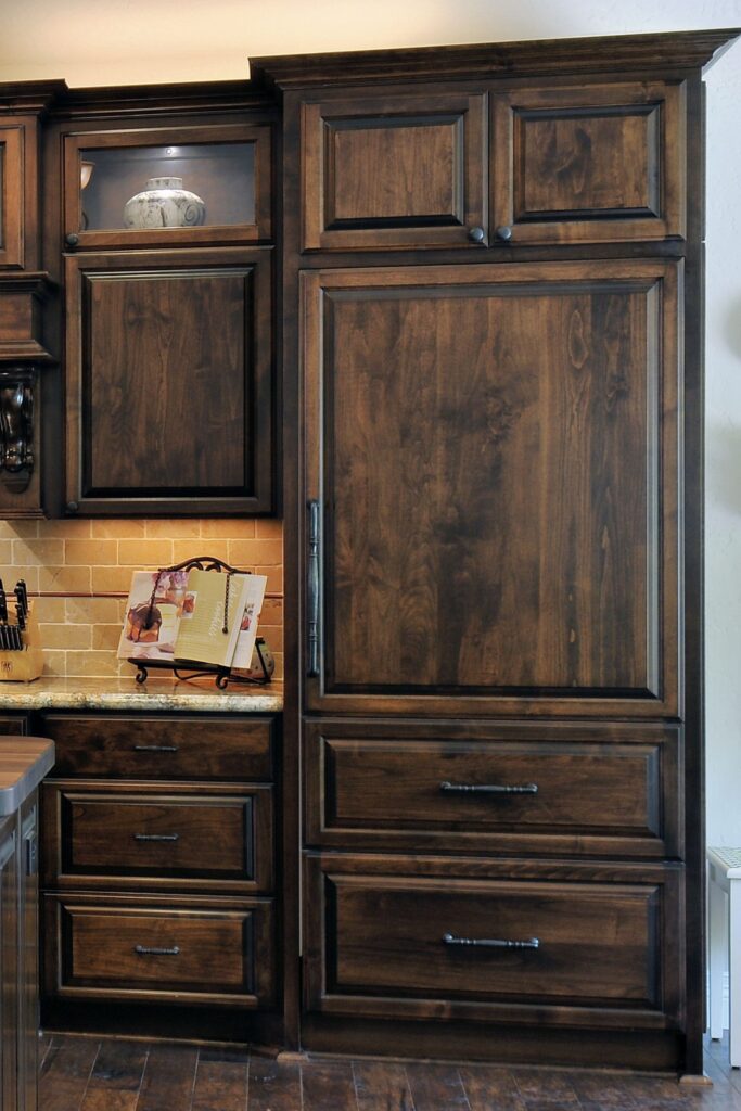 Tall paneled kitchen cabinetry with integrated appliance storage, deep drawers and dark stained wood finish