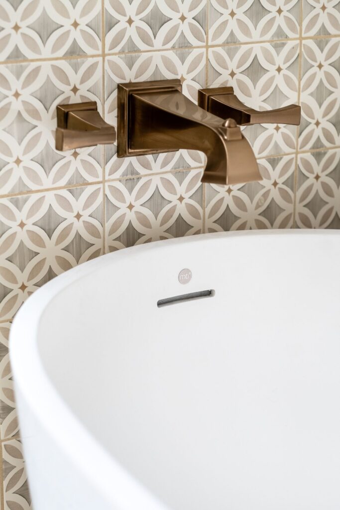 Wall-mounted bronze tub filler set against gray and white patterned bathroom tile