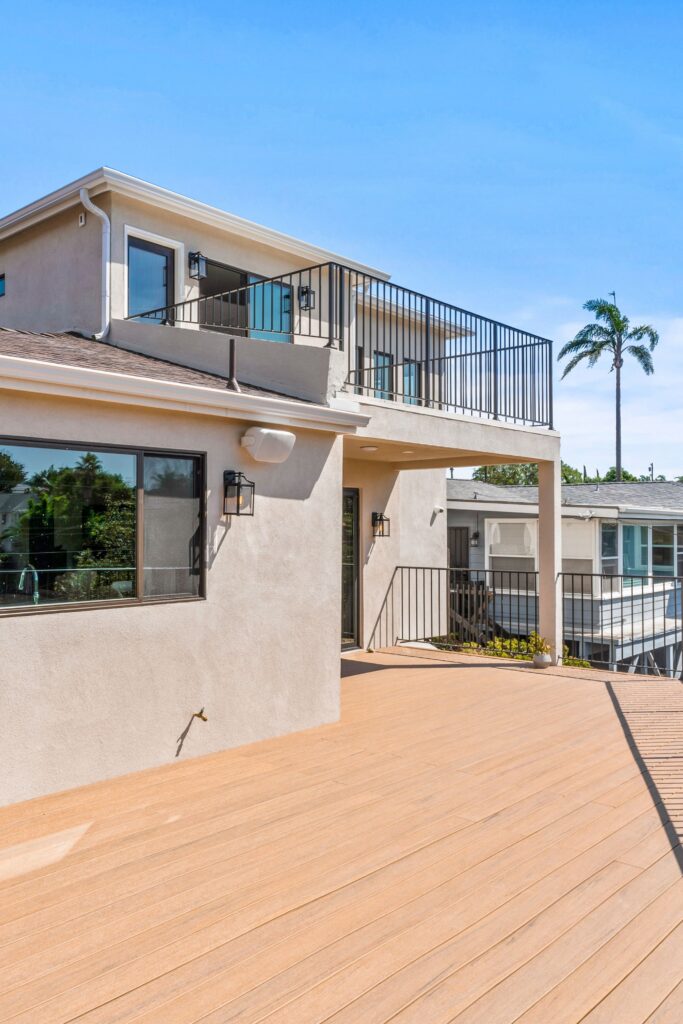 Large rear deck beneath second-story balcony with stucco exterior and black metal railings