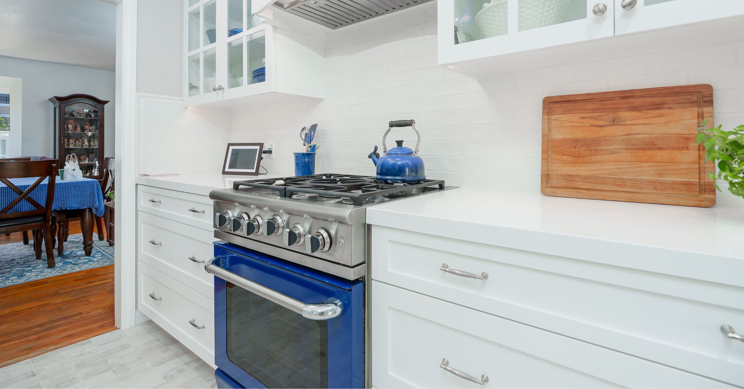 Blue range in white shaker kitchen with quartz counters, subway tile backsplash, and glass-front cabinets.