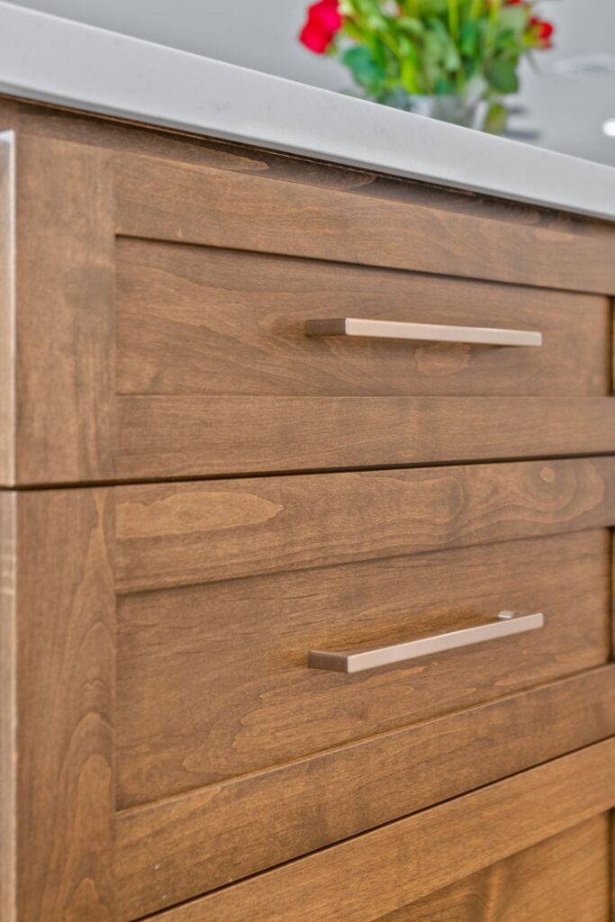 Close-up of stained wood island drawers with recessed panels, metal bar pulls and white countertop.