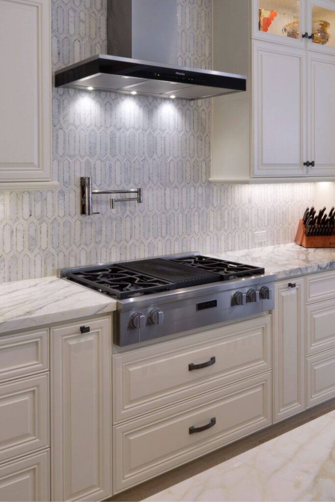 Del Mar kitchen cooktop wall with white cabinetry, stainless hood, veined counters and patterned tile backsplash