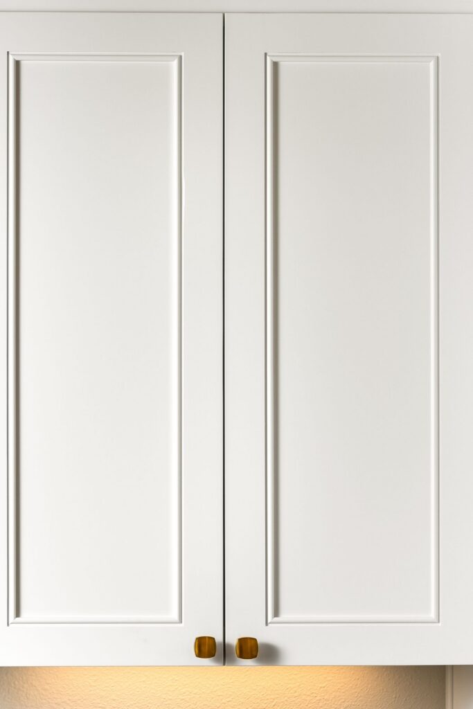 White raised-panel kitchen cabinet doors finished with small brushed brass knobs.