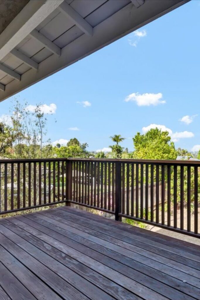 Covered wood deck with dark railing overlooking mature trees and surrounding Encinitas landscape.