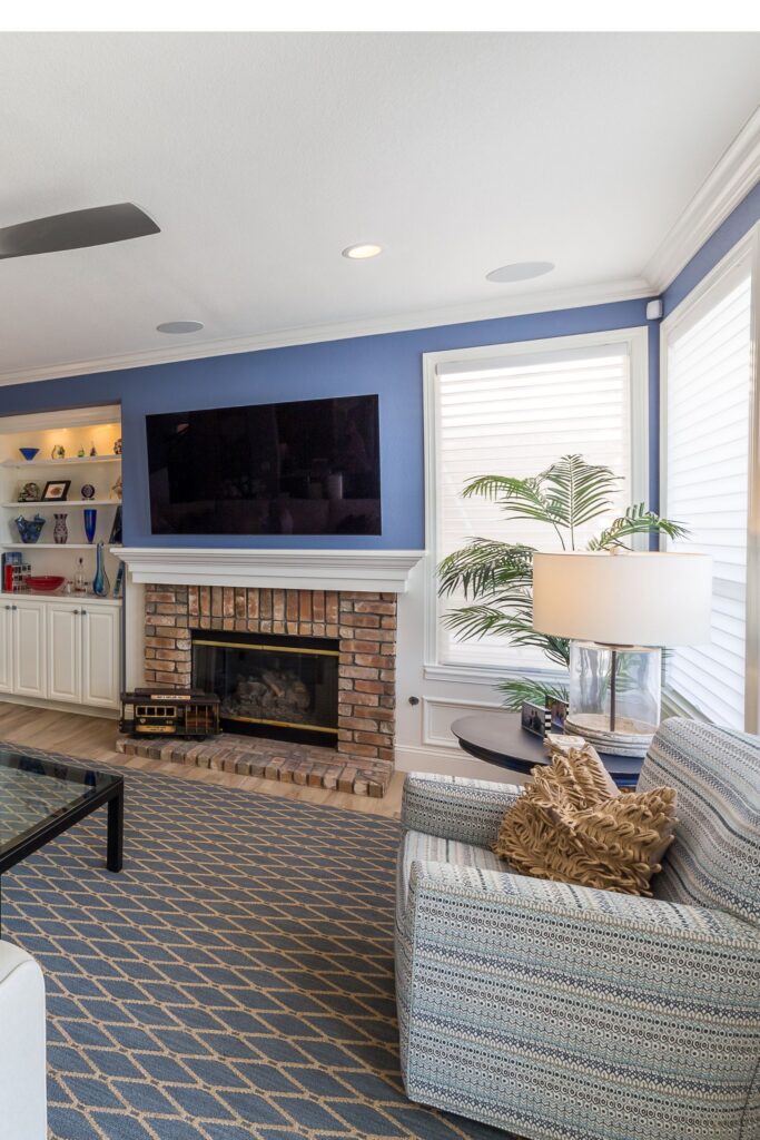 Family room with blue walls, white wainscoting, brick fireplace, built-in shelving and sectional seating.