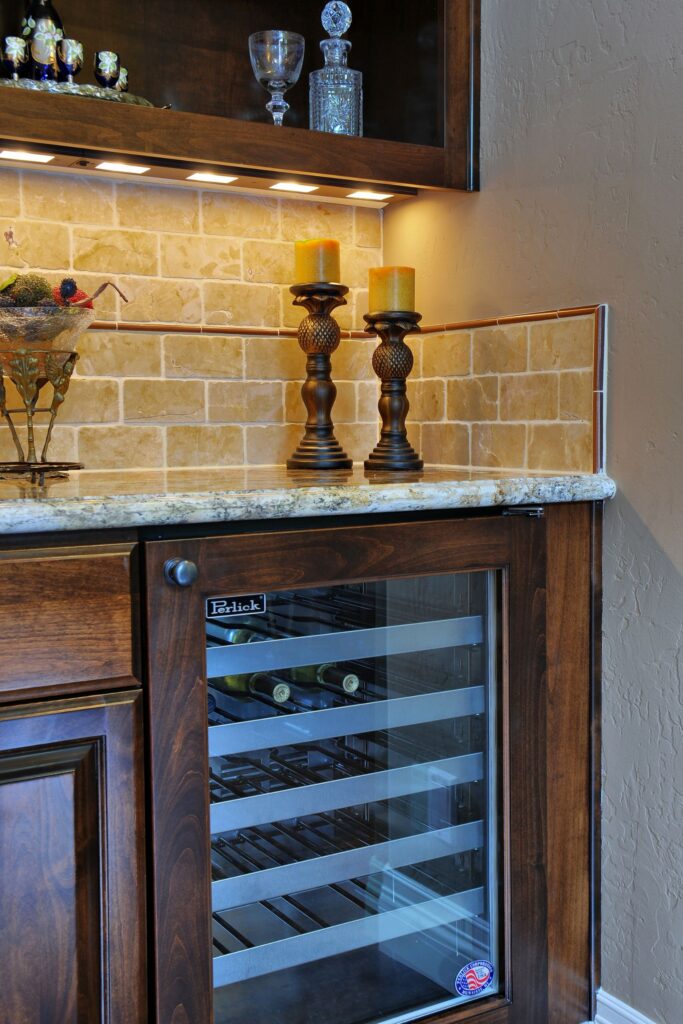 Wet bar with glass-front wine refrigerator, granite countertop, stone tile backsplash and illuminated display cabinet