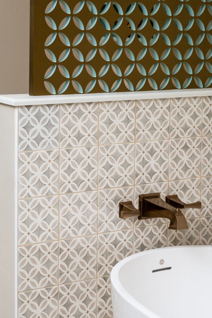Freestanding soaking tub with bronze wall-mounted filler, patterned tile surround and decorative screen