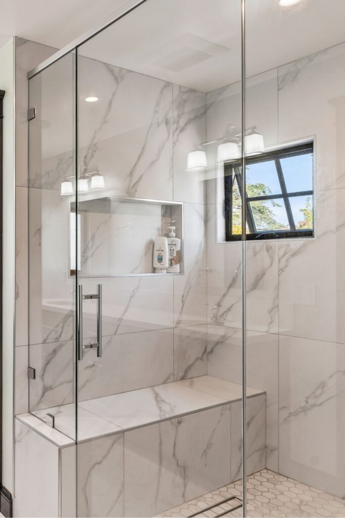 Glass-enclosed shower with marble-look wall tile, built-in bench, recessed niche and hex tile floor