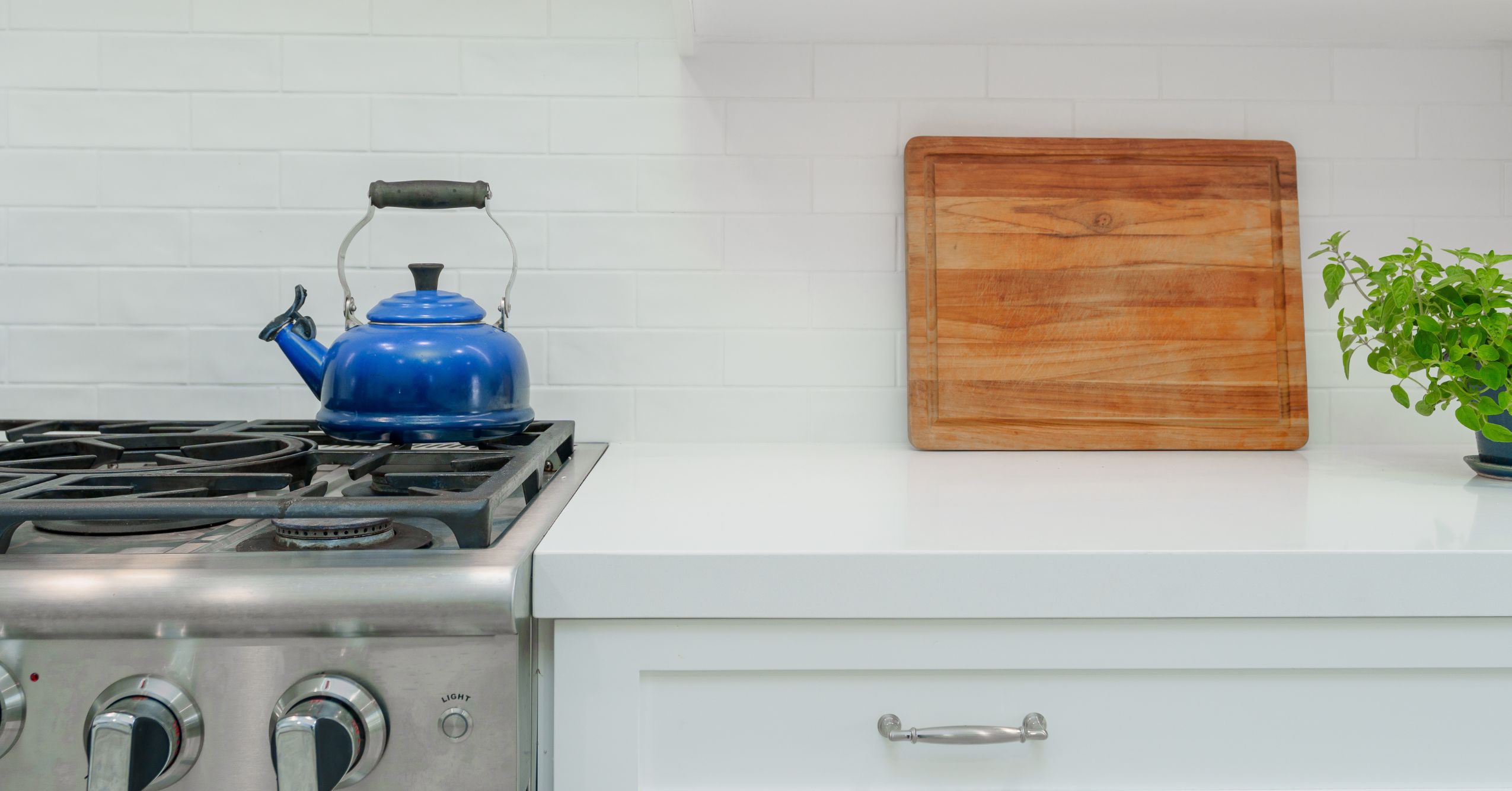 Blue gas range beside white quartz counter, shaker drawer front, and white subway tile backsplash.
