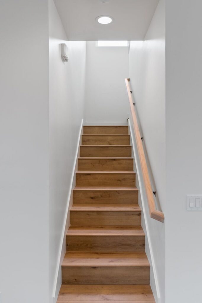 Wood staircase to the second floor with white walls, wood handrail, recessed lighting and skylight above.