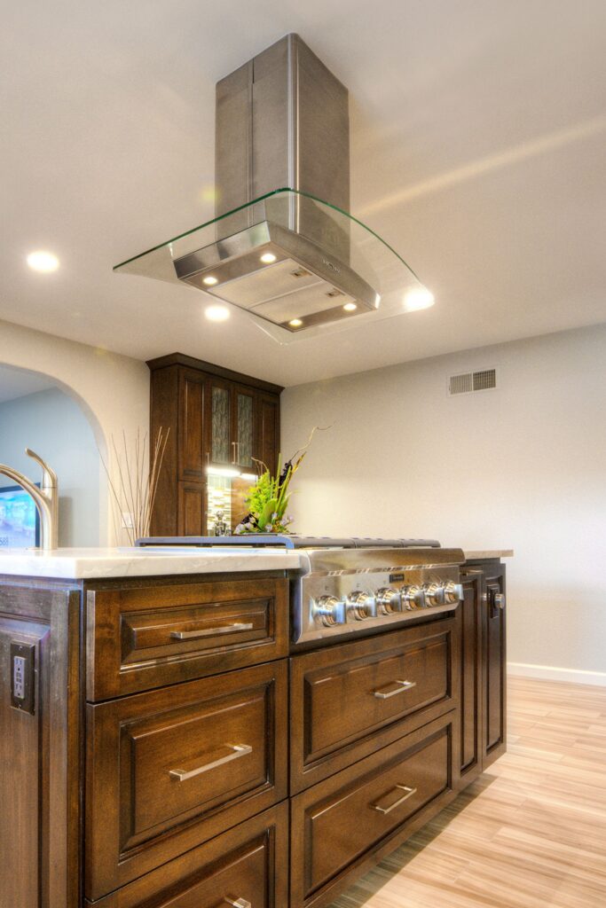 Island cooktop with stainless range, dark wood drawers and curved glass hood in a Mira Mesa kitchen remodel.