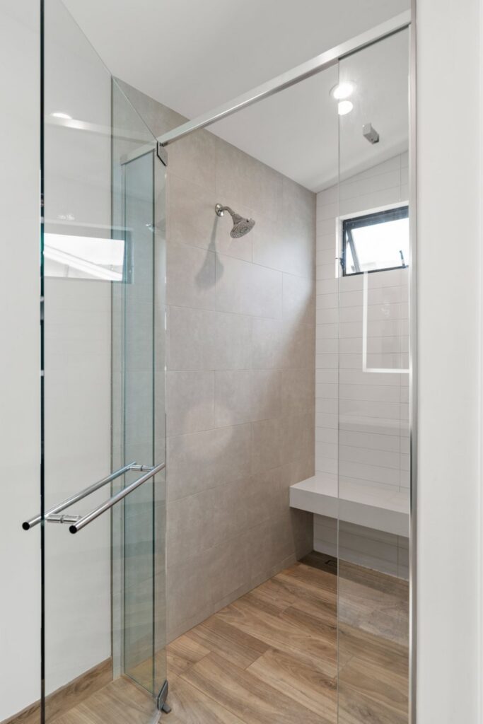 Walk-in shower with frameless glass, gray and white wall tile, built-in bench and black-framed window.