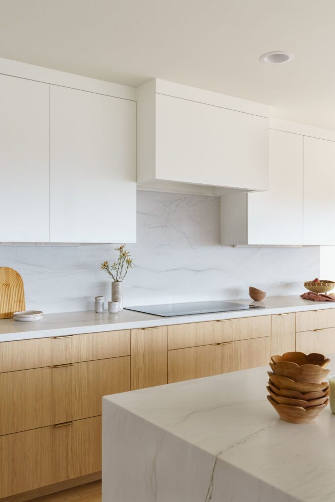 Kitchen cooktop wall with light wood base cabinets, white upper cabinetry and marble-look backsplash
