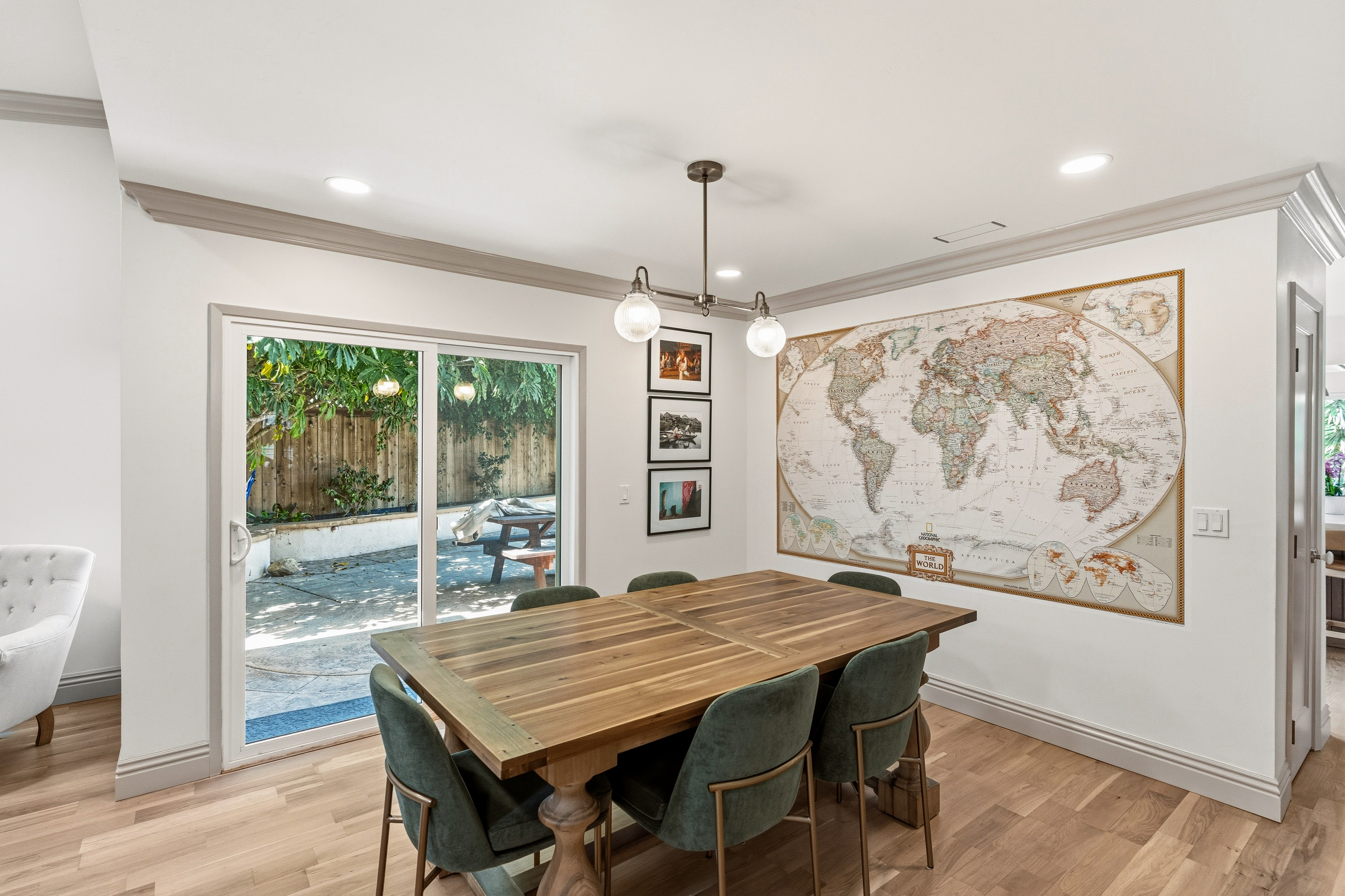 Dining room with wood table, green upholstered chairs, globe chandelier, hardwood flooring and patio doors.