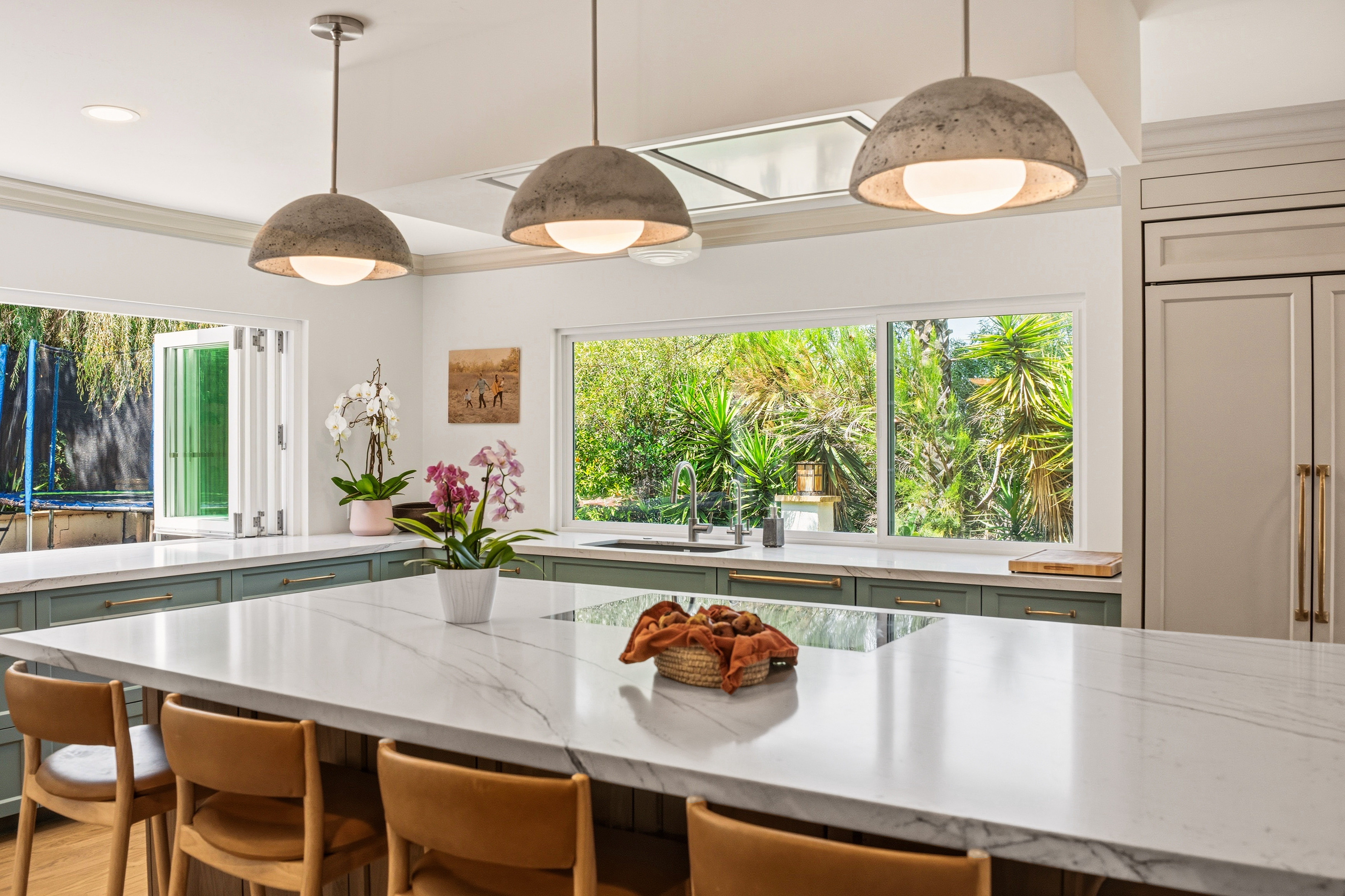Large kitchen island with marble-look counter, wood stools, concrete pendants and a ten-foot bi-fold window.