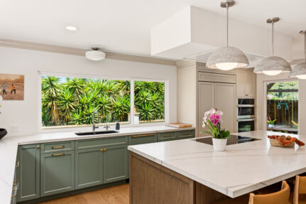 Open San Diego kitchen with sage cabinetry, wood island, white counters, pendant lights and a wide garden-facing window.
