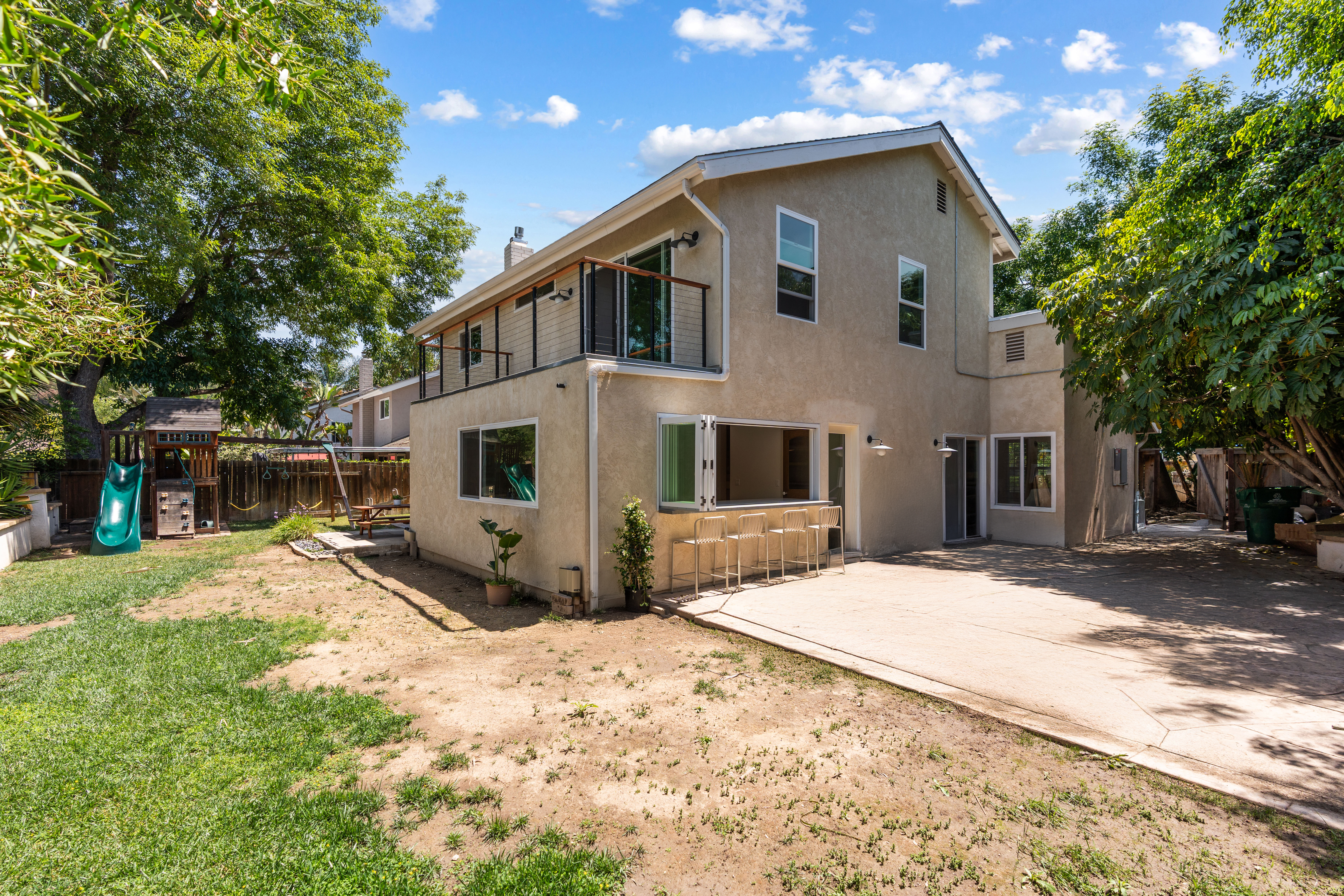 Rear exterior with second-story balcony, bi-fold kitchen window, outdoor counter, patio and family yard.